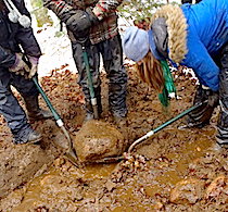 Students using shovels to lift a large rock into place for drainage on a trail
