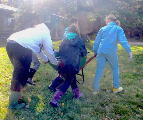 Students working together to move a wheelbarrow of wood chips for repairing a trail