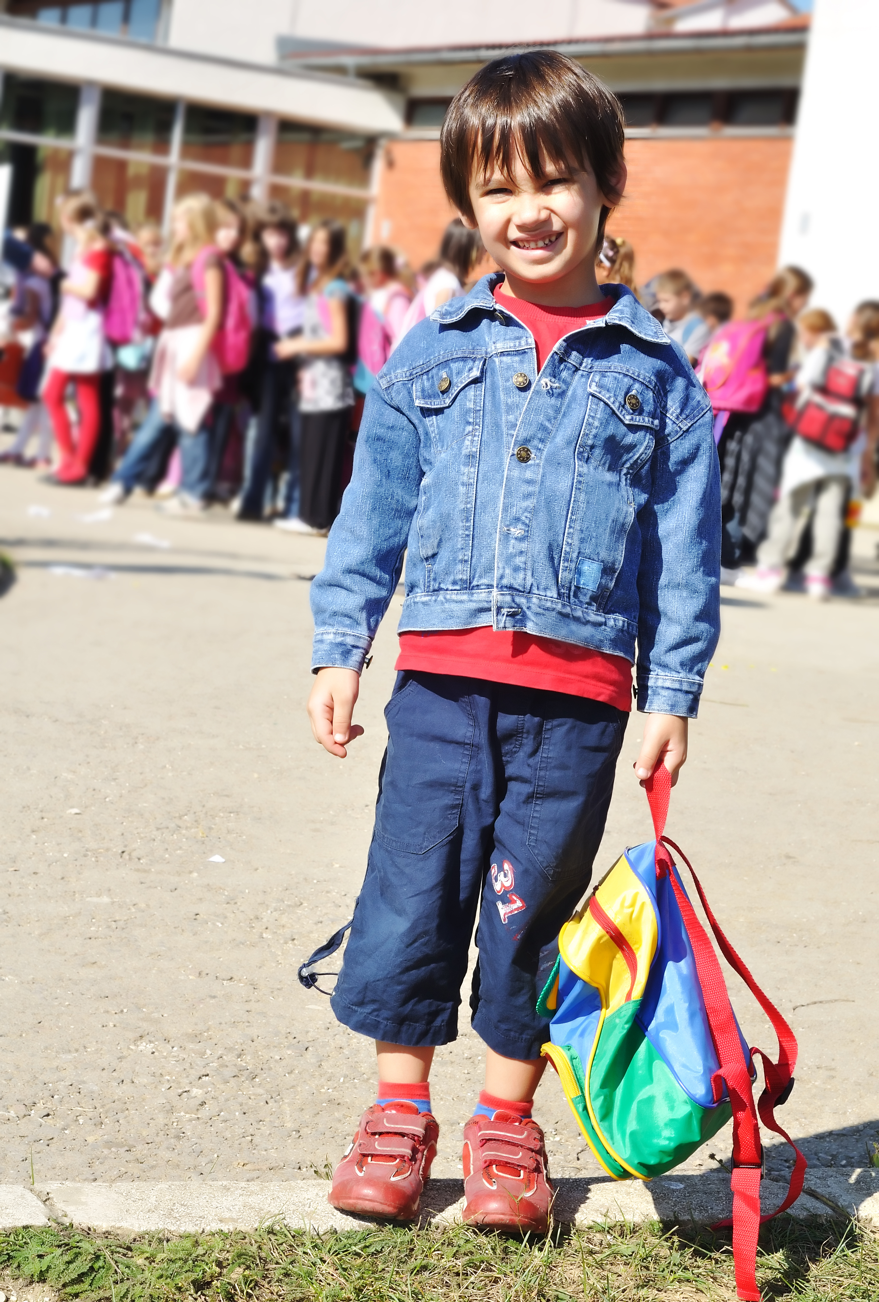 kindergarten student holds backpack and smiles while waiting to go into the school Open Gallery