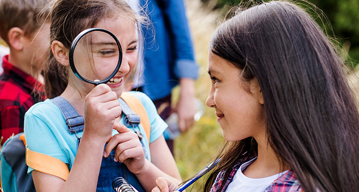 Two elementary students take a minute out of their nature explorations to have some fun with a magnifying glass