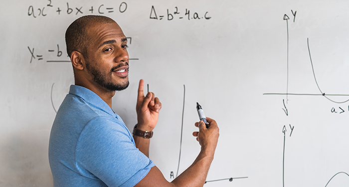 A math teacher presents to his class a white board upon which is written several formulae and graphs