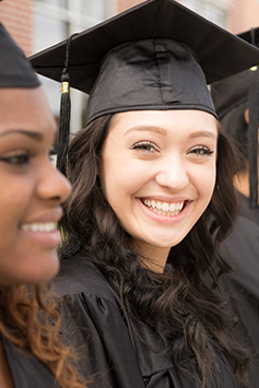 An elated female high school graduate poses with her graduation cap and gown