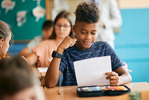 In a grade six classroom we see several students happily seated at their desks but none are so happy as the child in the middle as he looks down at a satisfactorily graded test