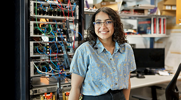 A female high school student stands proudly in front of a cable laden server