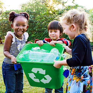 Three early elementary school students giggle as they attempt to sort recyclables