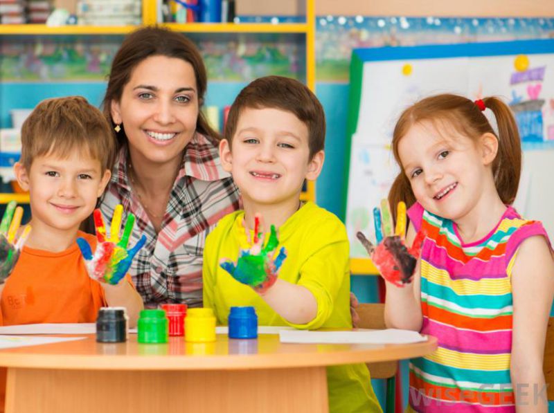 Teacher posing with students with hands dipped in multi-coloured paints