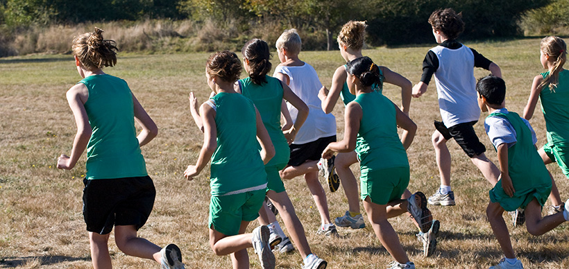 A pack of athletic students beginning their practice long distance run to the backdrop of a beautiful tree lined vista